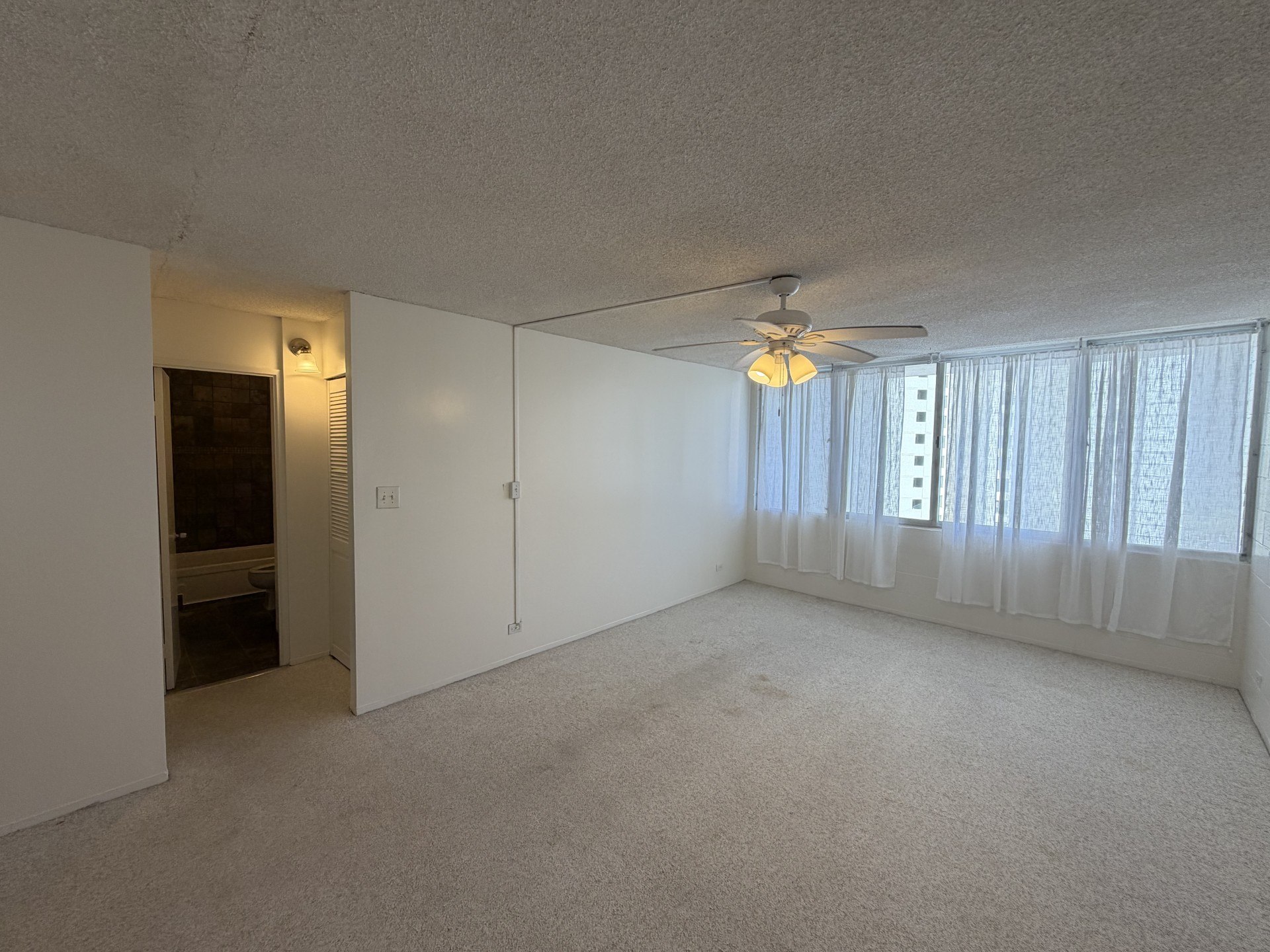 A room with a ceiling fan and a window with curtains.